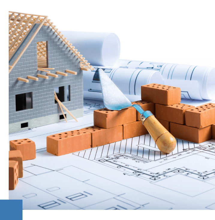Maquette de maison en construction, briques et truelle sur des plans